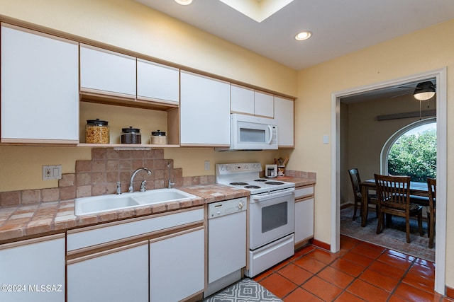 kitchen with dark tile patterned floors, sink, white cabinets, and white appliances