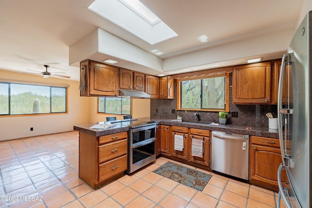 kitchen featuring kitchen peninsula, sink, a skylight, appliances with stainless steel finishes, and light tile patterned floors