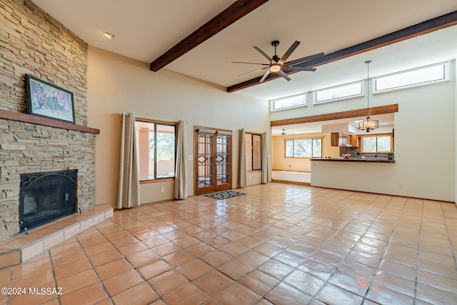 unfurnished living room with beamed ceiling, a stone fireplace, light tile patterned floors, french doors, and ceiling fan with notable chandelier