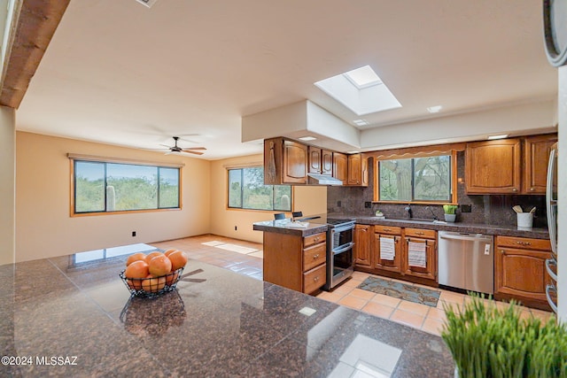 kitchen featuring backsplash, kitchen peninsula, sink, a skylight, and stainless steel appliances