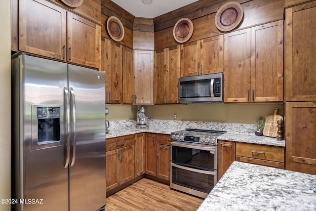 kitchen with light stone counters, stainless steel appliances, and light hardwood / wood-style flooring