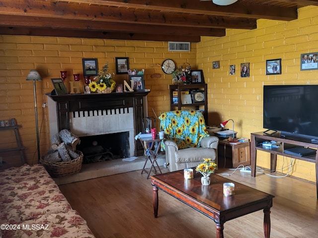 living room featuring wood-type flooring, a tile fireplace, and beamed ceiling