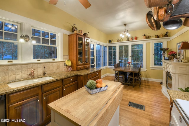 kitchen featuring light wood-type flooring, ceiling fan with notable chandelier, sink, a kitchen island, and tasteful backsplash