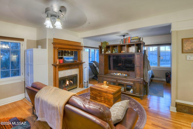 living room featuring ceiling fan, a tile fireplace, and light hardwood / wood-style floors