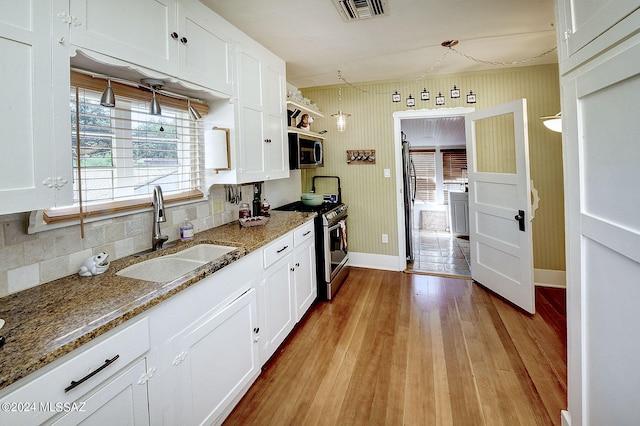 kitchen featuring light wood-type flooring, dark stone counters, sink, appliances with stainless steel finishes, and white cabinets