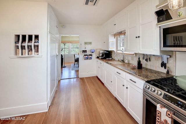 kitchen featuring gas stove, tasteful backsplash, light hardwood / wood-style floors, white cabinetry, and dark stone countertops