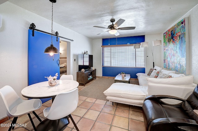 tiled living room with a textured ceiling, ceiling fan, and a barn door