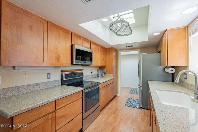 kitchen with light wood-type flooring, appliances with stainless steel finishes, light stone counters, and sink