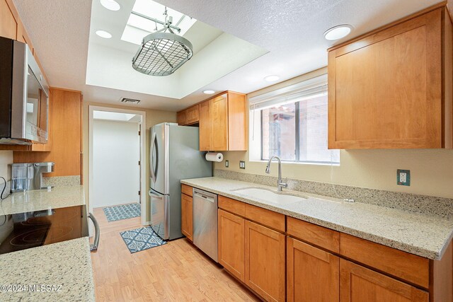 kitchen featuring light hardwood / wood-style floors, stainless steel appliances, sink, a skylight, and light stone counters