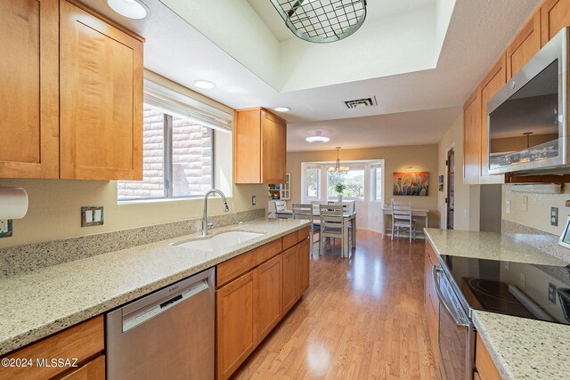 kitchen with light hardwood / wood-style flooring, sink, light stone countertops, hanging light fixtures, and appliances with stainless steel finishes