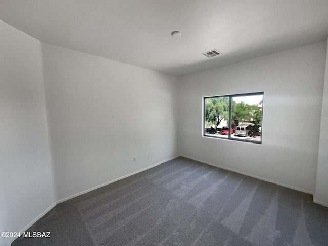 spare room with baseboards, visible vents, and dark carpet
