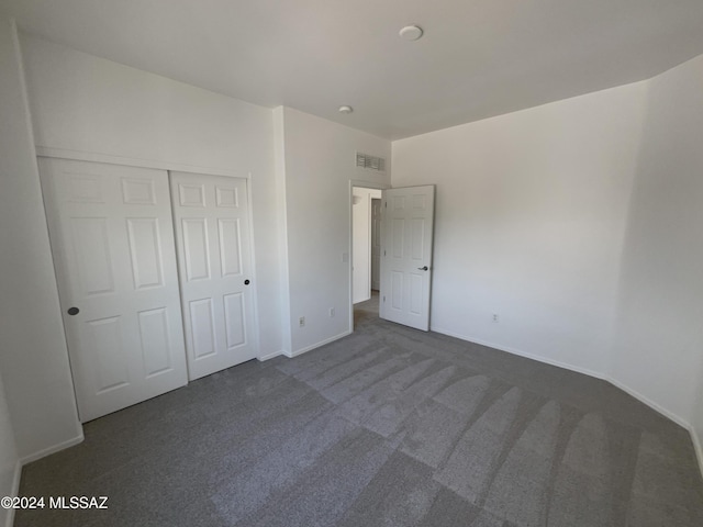 unfurnished bedroom with a closet, visible vents, baseboards, and dark colored carpet