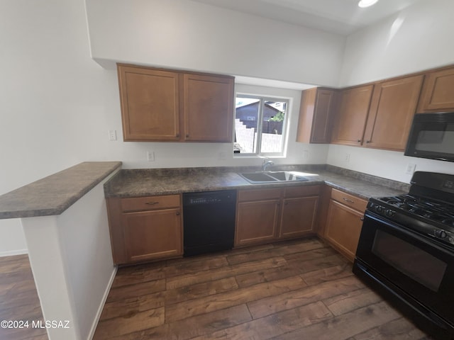 kitchen with dark countertops, a peninsula, black appliances, and a sink
