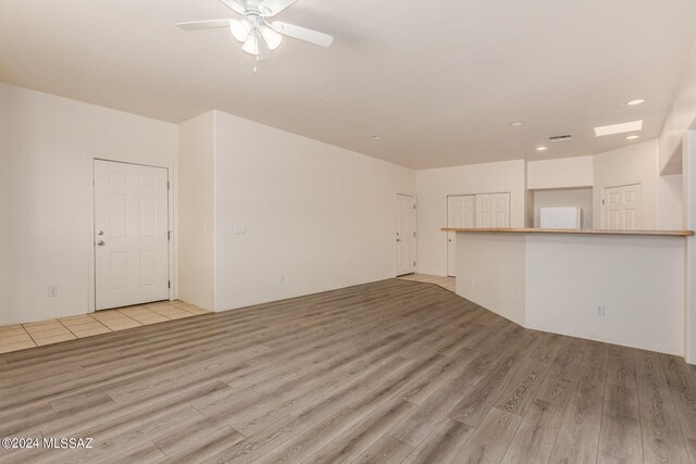 unfurnished living room featuring a skylight, ceiling fan, and light hardwood / wood-style floors