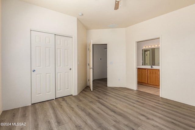 unfurnished bedroom with a closet, connected bathroom, sink, ceiling fan, and light wood-type flooring