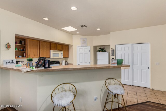 kitchen with a kitchen bar, kitchen peninsula, white appliances, and light hardwood / wood-style floors