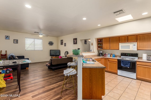 kitchen featuring light hardwood / wood-style flooring, white appliances, kitchen peninsula, ceiling fan, and a breakfast bar