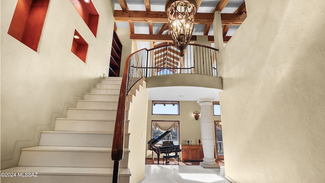 staircase with arched walkways, an inviting chandelier, a towering ceiling, beam ceiling, and ornate columns