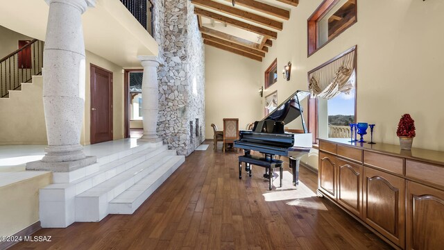 interior space with dark hardwood / wood-style floors, beamed ceiling, high vaulted ceiling, and ornate columns