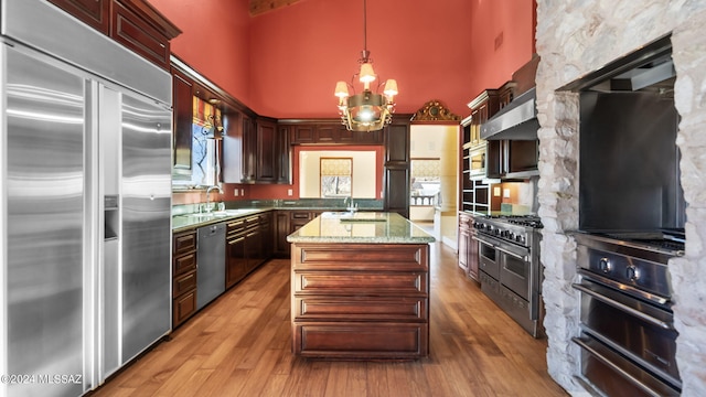 kitchen featuring a warming drawer, light wood-type flooring, a towering ceiling, a chandelier, and built in appliances