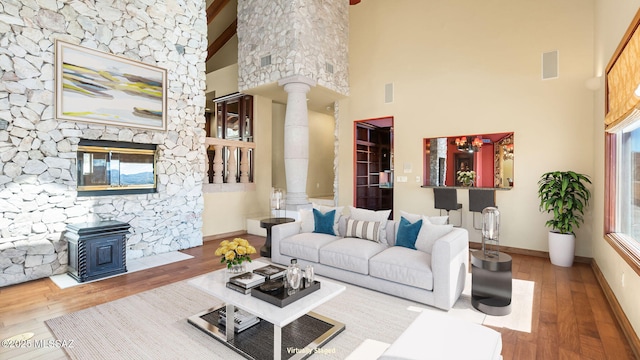 living area featuring a high ceiling, ornate columns, wood finished floors, a wood stove, and baseboards