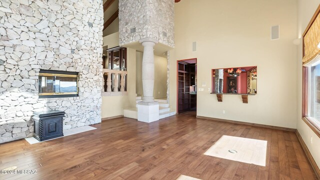 unfurnished living room featuring high vaulted ceiling, wood-type flooring, a fireplace, and decorative columns