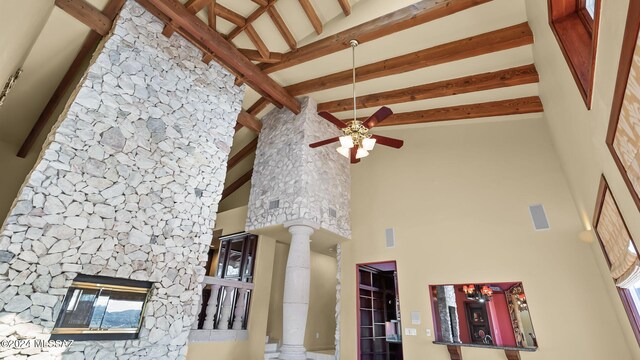 details featuring ceiling fan, beamed ceiling, a stone fireplace, and ornate columns