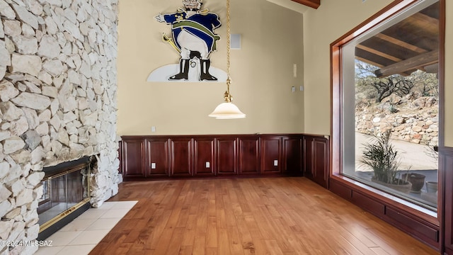 unfurnished living room featuring a wainscoted wall, a stone fireplace, and light wood finished floors