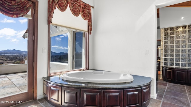 bathroom with a mountain view, a garden tub, stone finish flooring, and plenty of natural light