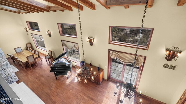 living room with a wealth of natural light, a high ceiling, hardwood / wood-style floors, and beam ceiling