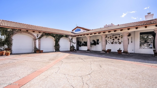 mediterranean / spanish-style home with a tile roof, aphalt driveway, a chimney, a garage, and stucco siding