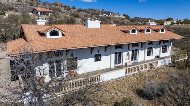 rear view of house featuring a tiled roof, a chimney, stucco siding, and a mountain view