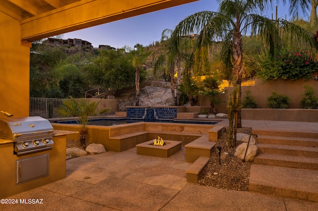 patio terrace at dusk featuring exterior kitchen, a grill, and an outdoor fire pit