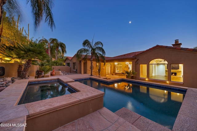 pool at dusk featuring an in ground hot tub and a patio area