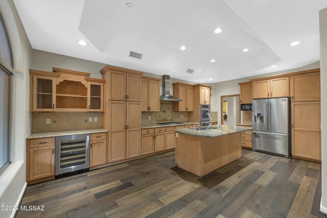 kitchen with wine cooler, dark wood-type flooring, wall chimney exhaust hood, stainless steel appliances, and a center island with sink