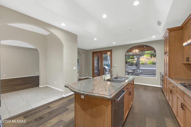 kitchen with light stone countertops, stainless steel appliances, hardwood / wood-style flooring, a center island with sink, and sink