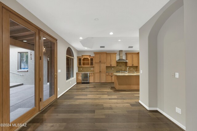 kitchen with beverage cooler, dark wood-type flooring, wall chimney range hood, and tasteful backsplash