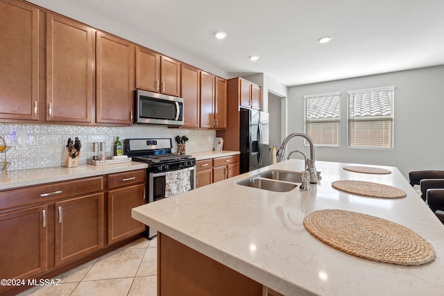 kitchen with sink, a center island with sink, stainless steel appliances, light stone countertops, and decorative backsplash