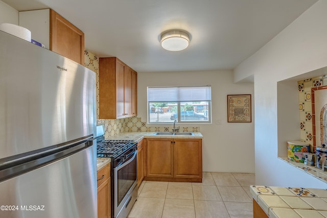 kitchen featuring backsplash, tile counters, stainless steel appliances, sink, and light tile patterned flooring