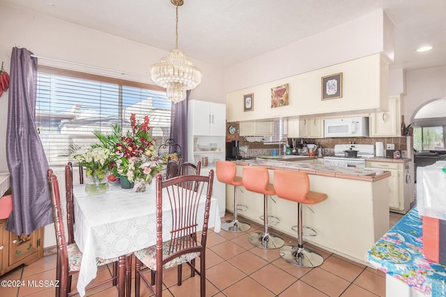 kitchen with an inviting chandelier, light tile patterned floors, pendant lighting, white appliances, and decorative backsplash