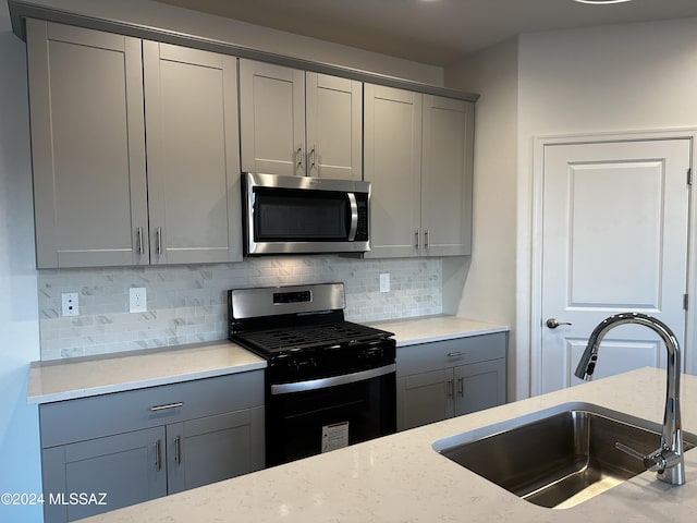 kitchen with gray cabinetry, sink, light stone countertops, tasteful backsplash, and stainless steel appliances