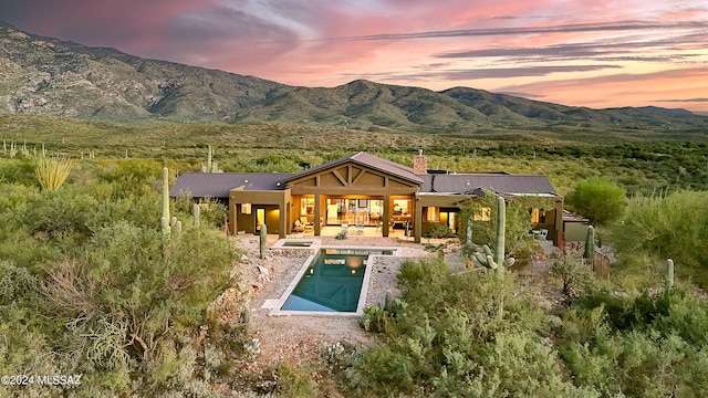 back of house at dusk featuring a patio, a chimney, a mountain view, and an outdoor pool