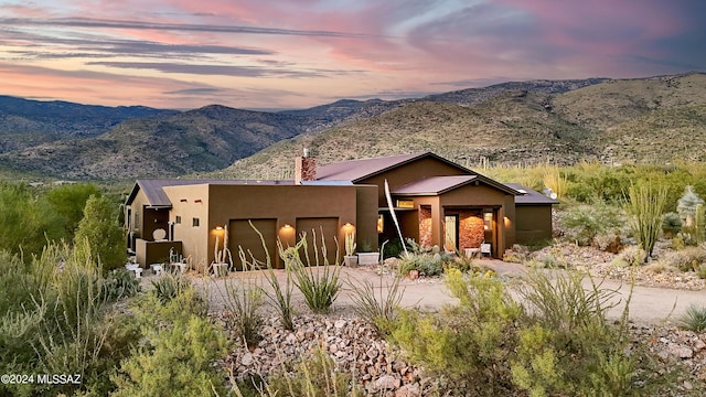 pueblo-style house with driveway, stucco siding, a mountain view, and an attached garage
