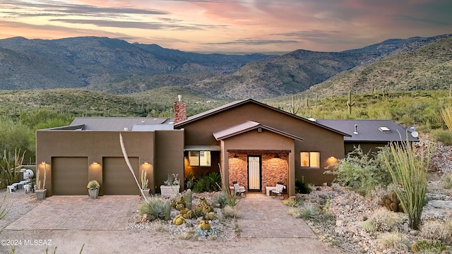 view of front facade with decorative driveway, a mountain view, an attached garage, and stucco siding