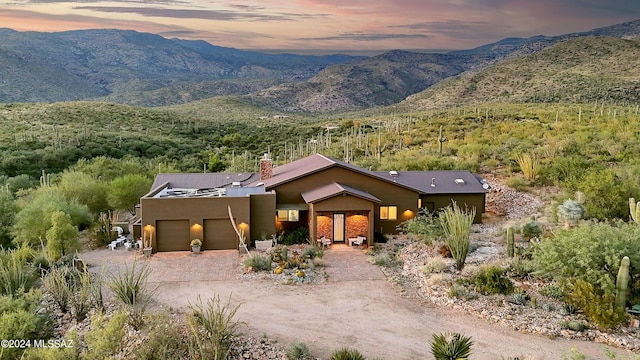 view of front facade with an attached garage, a mountain view, decorative driveway, stucco siding, and a chimney