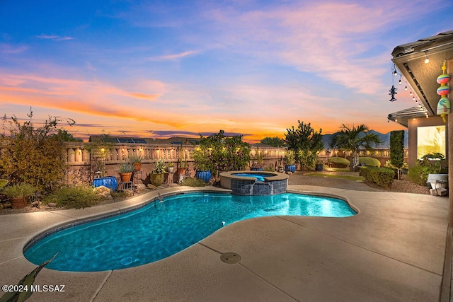 pool at dusk featuring an in ground hot tub and a patio area