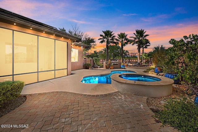 pool at dusk featuring a patio and an in ground hot tub