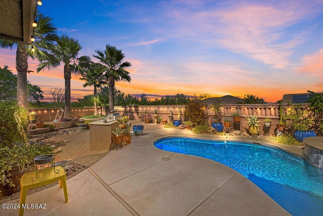 pool at dusk with a patio and pool water feature