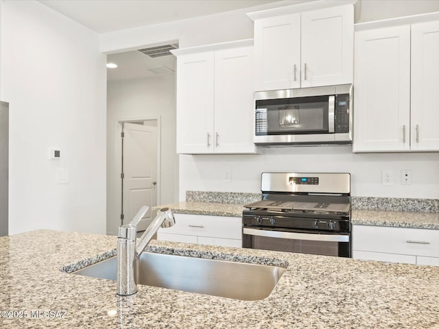kitchen featuring white cabinets, light stone countertops, appliances with stainless steel finishes, a sink, and visible vents