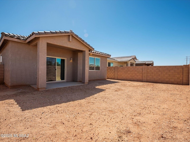 rear view of property with a tile roof, a fenced backyard, a patio area, and stucco siding